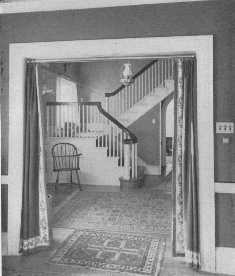 This attractive Colonial hallway shows a good arrangement
of rugs. The border on the portières spoils the effect, but the lamp is
well chosen.